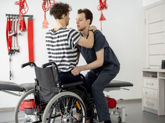 Asistent pomaga invalidu na vozičku vstati.