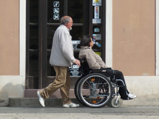 Asistent po pločniku poganja voziček na katerem je invalid